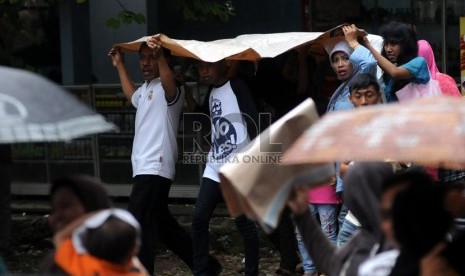  Wisatawan berlindung dari hujan dengan menggunakan alat seadanya saat berkunjung ke Kebun Binatang Ragunan, Jakarta, Selasa (25/12). (Republika/Aditya Pradana Putra)