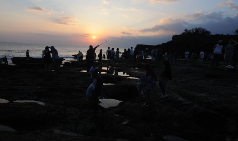 Wisatawan menikmati pemandangan matahari terbenam (sunset) di kawasan Wisata Pura Tanah Lot, Tabanan, Bali, Jumat (5/7/2019).