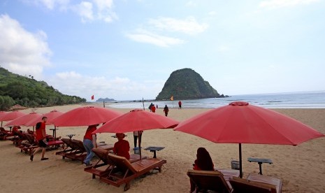 Wisatawan menikmati suasana pantai dengan latar belakang Pulau Merah di Banyuwangi, Jawa Timur, Jumat (7/12/2018). Pulau Merah yang tercipta dari magma gunung api purba itu, telah ditetapkan sebagai situs Geopark Nasional.