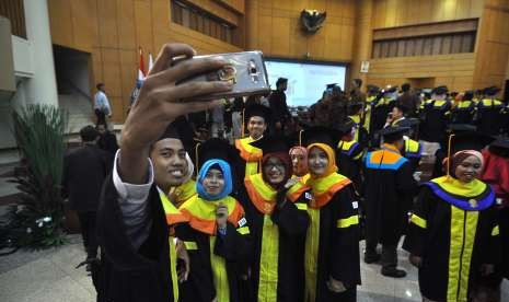 Wisudawan dan wisudawati berswafoto seusai mengikuti proses penyerahan ijazah. Universitas merupakan salah satu sumber pengembangan sumber daya manusia (SDM).