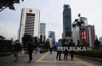 Sejumlah pekerja berjalan usai bekerja dengan latar belakang gedung perkantoran di Jl Jenderal Sudirman, Jakarta, Kamis (16/4/2020). Pemprov DKI Jakarta akan memberikan saksi berupa mencabut perizinan kepada perusahaan yang tetap beroperasi di masa Pembatasan Sosial Berskala Besar (PSBB) kecuali delapan sektor yang memang diizinkan