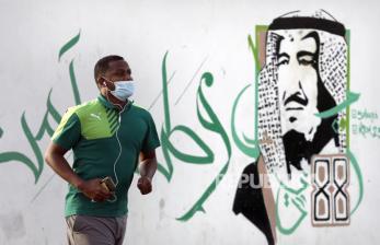 Dokter Terkemuka Arab Saudi Dirawat karena Covid-19. Seorang pria memakai masker saat melewati mural Raja Salman di Saudi Arabia, Ahad (28/6). Kasus COVID-19 di dunia mencatatkan angka tertinggi dalam 24 jam terakhir pada Ahad (28/6),  dengan jumlah lebih dari 10 juta kasus positif dan 500.000 kematian. (AP Photo/Amr Nabil)
