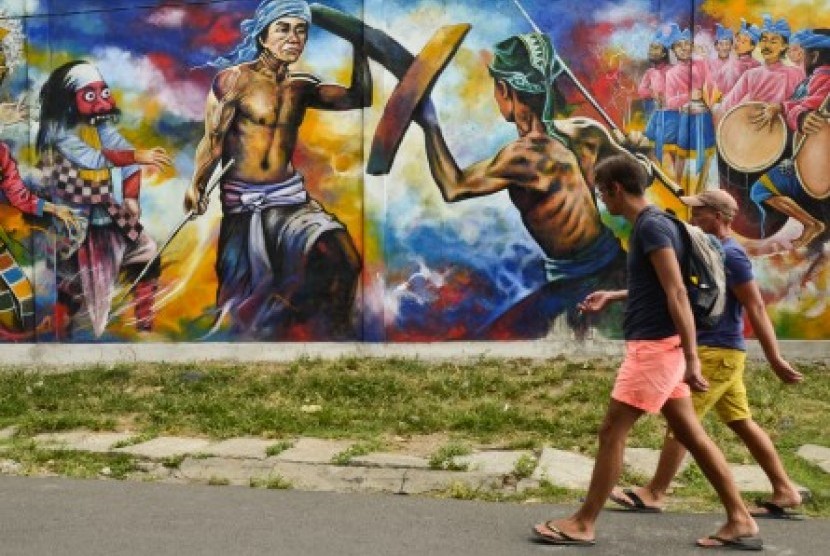 (Ilustrasi) Dua orang wisatawan asing melintas di dekat tembok mural bertemakan atraksi budaya 