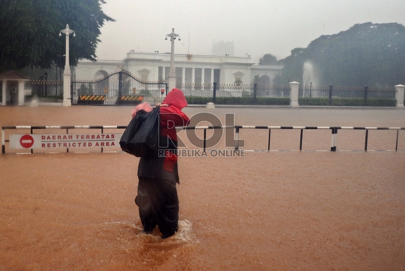 ?Warga melintasi genangan air saat hujan menguyur kawasan depan Istana Merdeka di Jl Merdeka Barat, Jakarta, Senin (9/2).   (Republika/Tahta Aidilla)