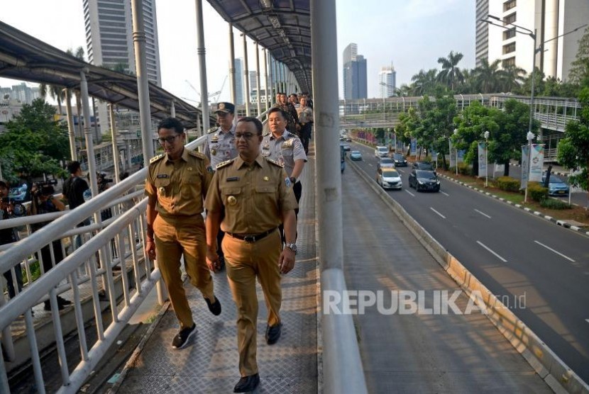 Gubernur DKI Jakarta Anies Baswedan dan Wakil Gubernur Sandiaga Uno berjalan ketika hendak menaiki bus Transjakarta di Halte Dukuh Atas, Jakarta, Selasa (17/10).