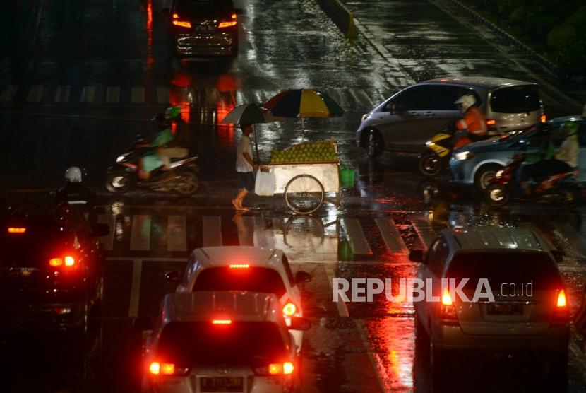 Pedagang menyeberangi pelican crossing menggunakan payung saat hujan di Jakarta, Selasa (27/11).