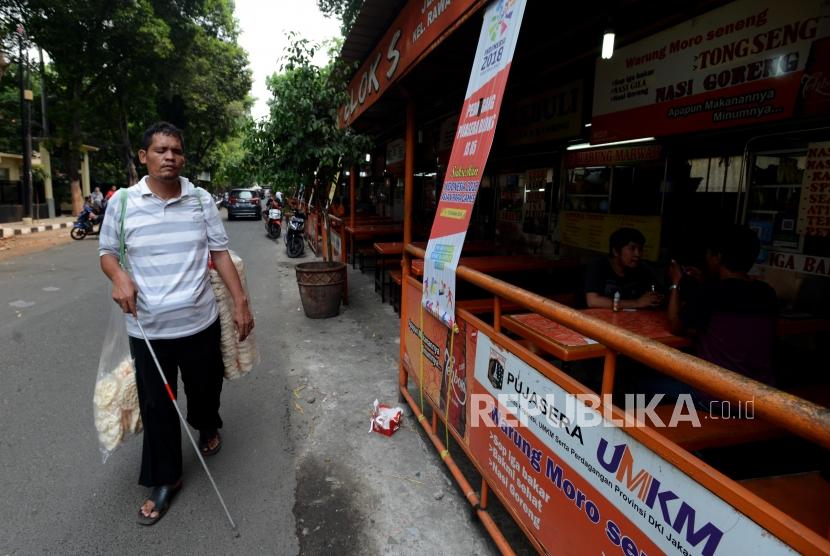 Robin (41) penjual kerupuk penyandang tuna netra berjalan untuk menjual kerupuknya di kawasan Blok S, Kebayoran Baru, Jakarta Selatan, Kamis (18/10).