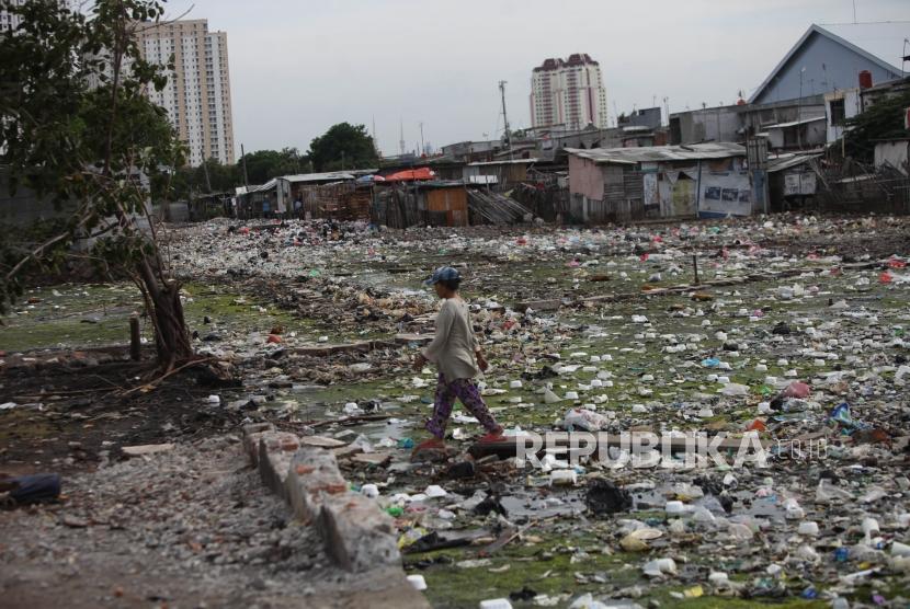 Warga melintasi diantara tumpukan sampah di pemukiman penduduk Kawasan Muara Baru, Jakarta, Kamis (28/12).