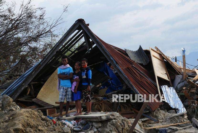 Satu keluarga berdiri di depan rumahnya yang rubuh di  wilayah Petobo, Kabupaten Sigi, Sulawesi Tengah, Kamis (11/10).