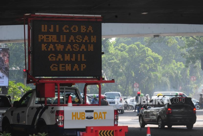 Kendaraan melintas di dekat papan sosialisasi uji coba perluasan ganjil genap di kawasan Pancoran, Jakarta Selatan, Senin (2/7).