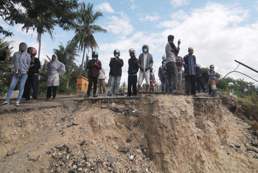 Warga berdiri di jalan batas kampung yang hilang terseret liquifaksi atau pencairan tanah akibat gempa bumi di Desa Jono Oge, Sigi, Sulawesi Tengah, Senin (8/10).