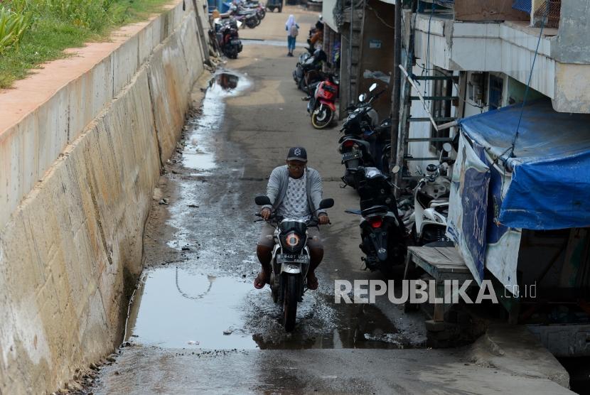 Pengendara motor melintasi genangan dari air yang mengucur dari tanggul pengaman pantai yang bocor di kawasan Muara Baru, Jakarta, Selasa (11/12).