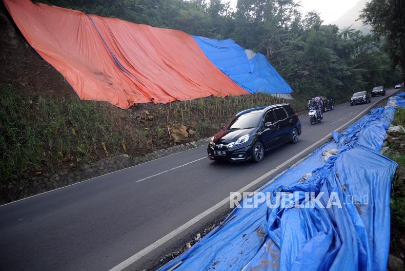 Kendaraan melintas di dekat bekas longsoran tebing yang ditutupi terpal di kawasan Puncak, Bogor, Jawa Barat, Sabtu (9/6).