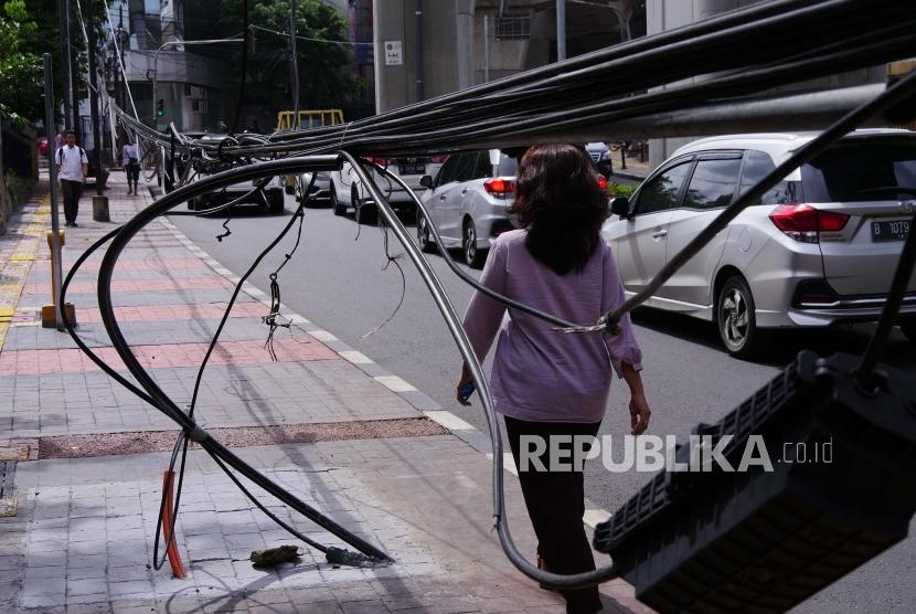 Pejalan kaki melintasi kabel serat optik yang menjuntai di jalan. ilustrasi