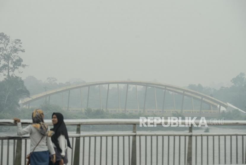 Warga beraktivitas dengan latar belakang aliran Sungai Siak yang diselimuti asap kebakaran lahan gambut di Alun-alun Kabupaten Siak, Riau, Kamis (12/9).