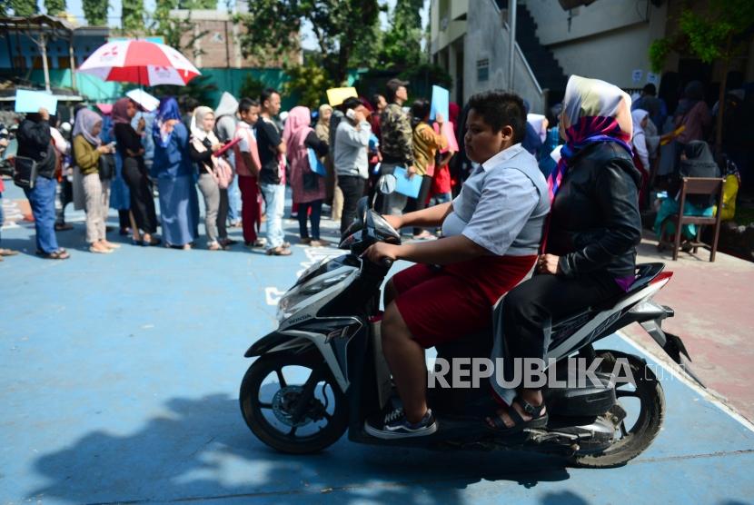 Seorang siswa berseragam sekolah dasar membawa sepeda motor ke sekolah dengan membonceng ibunya (ilustrasi).