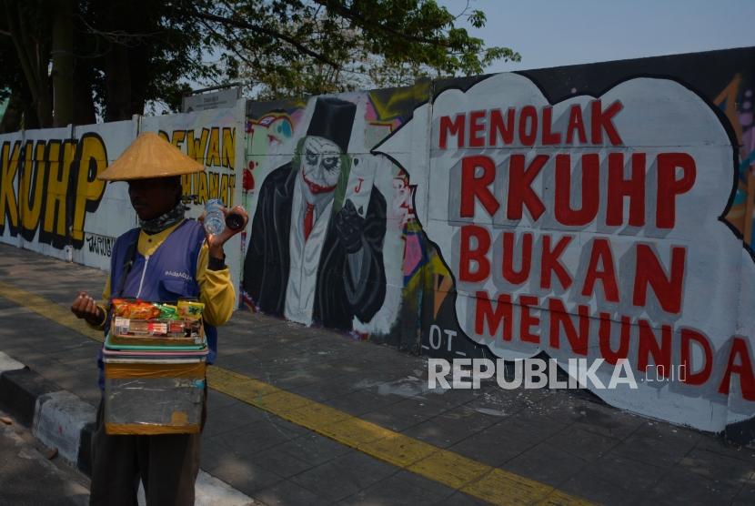 Warga melintas di area mural Tolak RUU RKUHP di Rawamangun, Jakarta Timur. 