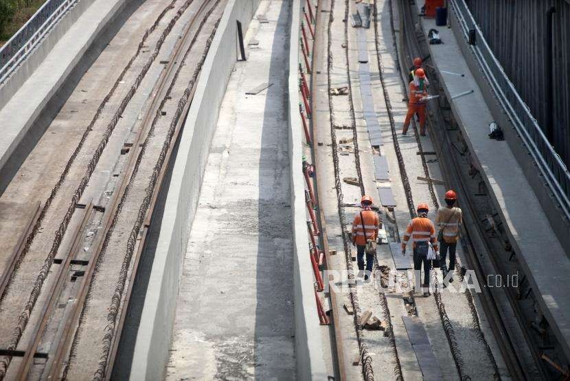 Pekerja berjalan saat menyelesaikan pemasangan rel Kereta Light Rail Transit (LRT) Jabodebek di kawasan Kampung Makassar, Jakarta,  Selasa (28/8).