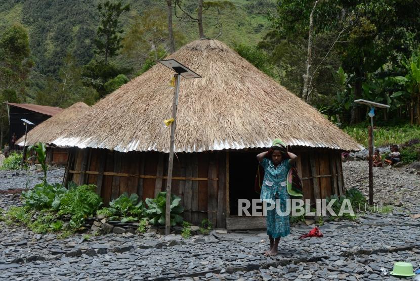 Warga beraktivitas di dekat rumah adat honai yang telah terpasang  jaringan Lampu Tenaga Surya Hemat Energi (LTSHE ) di Kabupaten Puncak Jaya, Papua, Jumat (15/3).