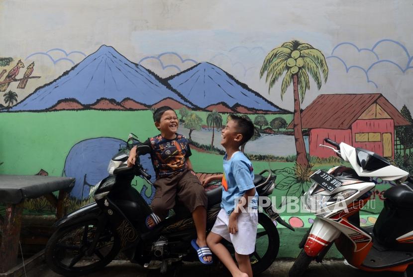 Anak-anak bermain di dekat tembok yang dihiasi mural di kawasan Jembatan Lima, Tambora, Jakarta Barat.