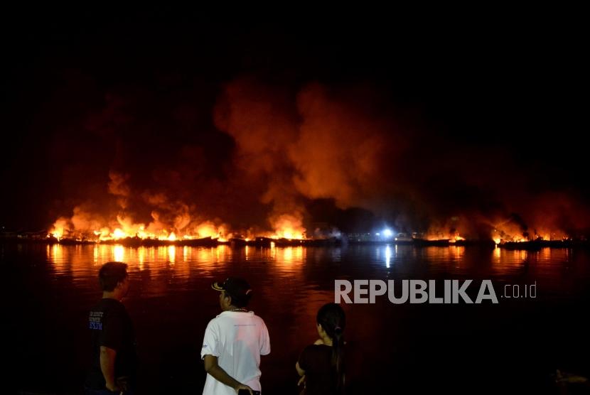Warga menyaksikan kapal yang terbakar di Pelabuhan Muara Baru, Jakarta, Sabtu (23/2).