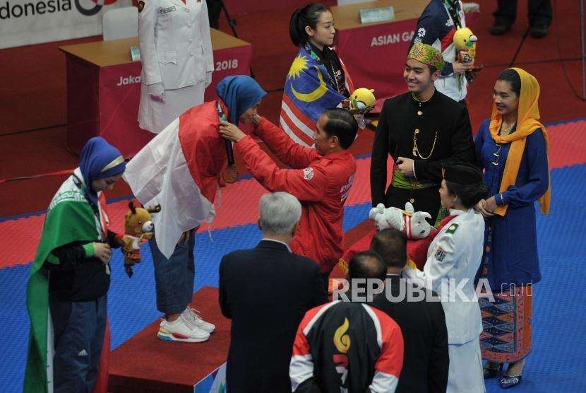 Presiden Joko Widodo memberikan medali emas kepada atlet taekwondo putri Indonesia Defia Rosmaniar saat penyerahan prosesi medali cabang taekwondo nomor poomsae Asian Games 2018 di Jakarta Convention Center, Senayan, Jakarta, Ahad (19/8).