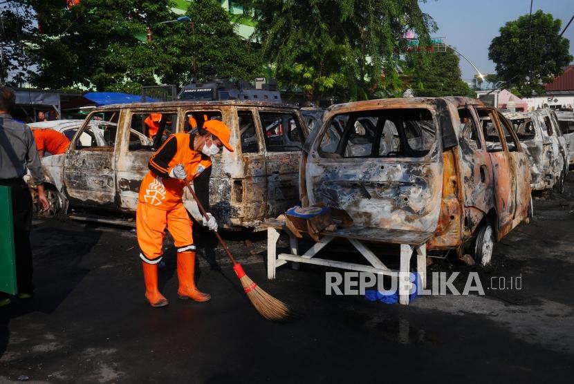 Petugas Dinas kebersihan menyapu serpihan bangkai mobil yang terbakar di area Kompleks Asrama Brimob Petamburan, Jakarta, Rabu (22/5).