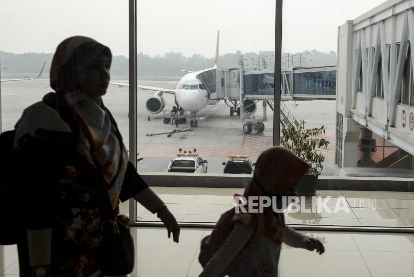 Dampak Corona, Penumpang Luar Negeri ke Pekanbaru Turun 50 Persen. Penumpang melintas dengan latar belakang pesawat yang diselimuti kabut asap di Bandara Sultan Syarif Kasim II Pekanbaru, Riau.