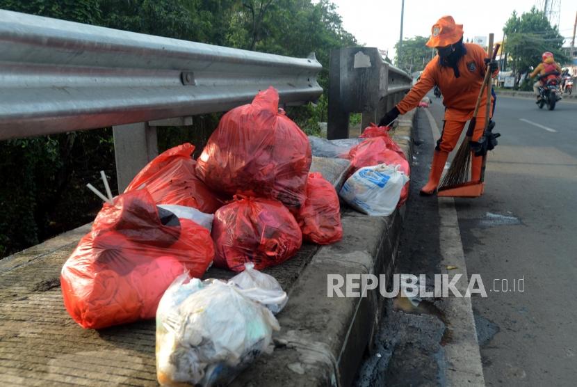 Petugas kebersihan membersihkan tumpukan plastik berisi sampah berada di pinggir Jalan Raya Bogor - Jakarta, Depok, Jawa Barat, Selasa (8/1).