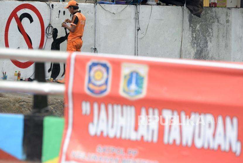 Petugas PPSU membuat mural di dekat spanduk bertuliskan himbauan stop tawuran di Kawasan Pasar Rumput, Jakarta, Rabu (29/8).