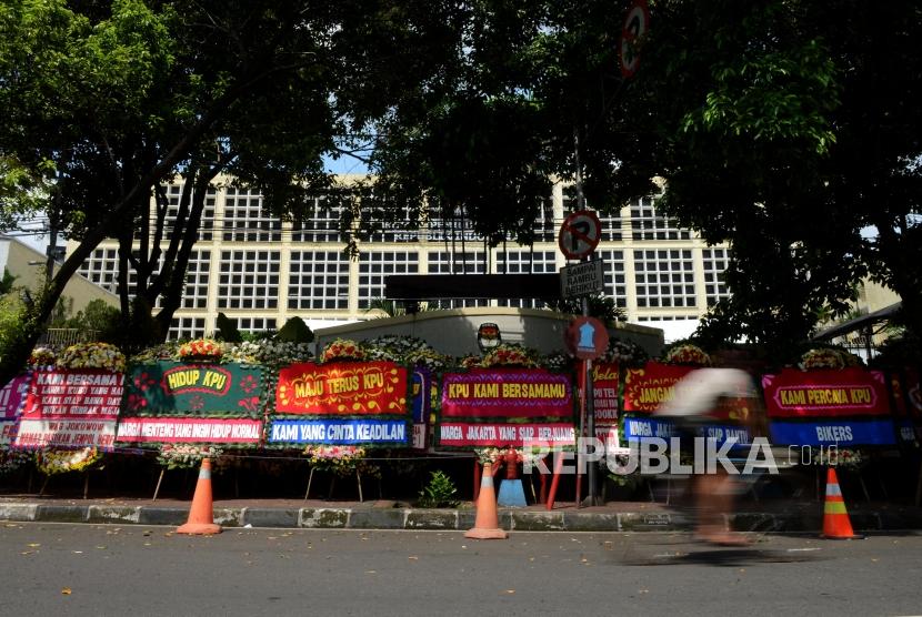 Pesepeda melintas di dekat karangan bunga yang terpasang di depan Gedung Komisi Pemilihan Umum (KPU), Jakarta, Ahad (21/4).