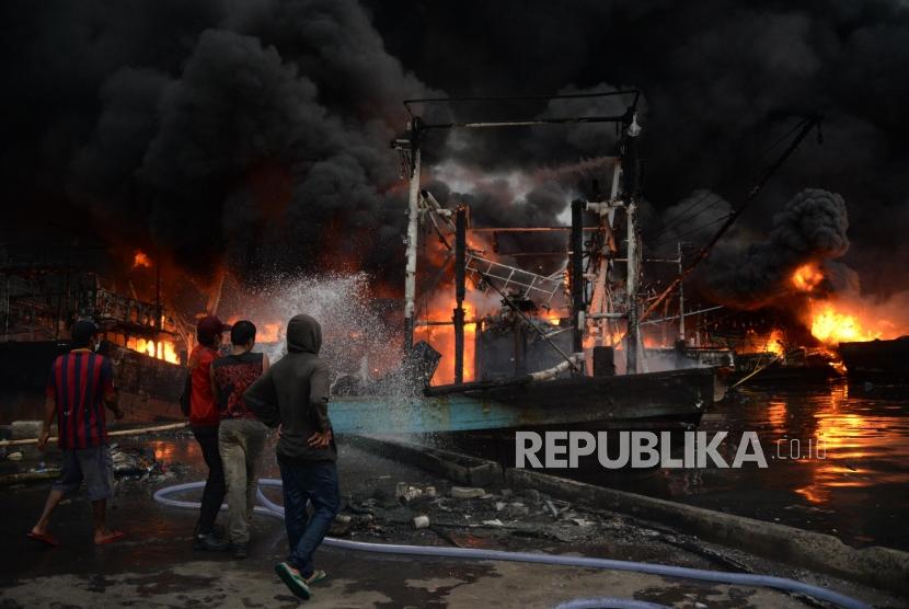 Sejumlah petugas pemadam kebakaran dibantu warga berusaha memadamkan kapal yang terbakar di Pelabuhan Muara Baru, Jakarta, Sabtu (23/2).
