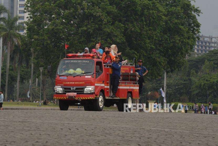 Pengunjung Kawasan Monumen menaiki kendaraan pemadam kebakaran di kawasan Monas Jakarta, Ahad (23/9).