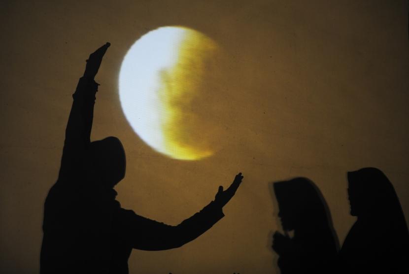 Warga berpose dengan latar gerhana bulan. 