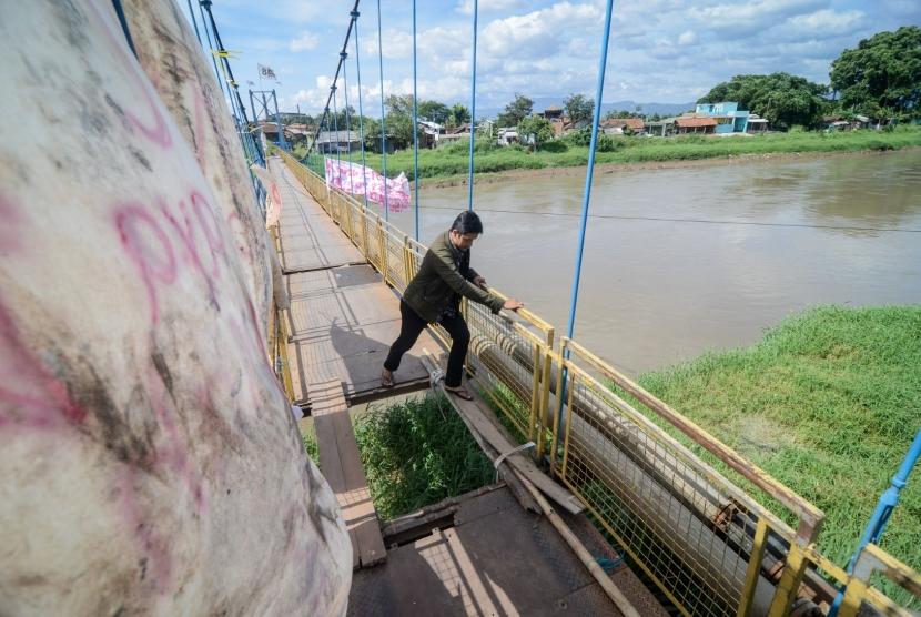 Warga menyeberangi Sungai Citarum menggunakan jembatan gantung yang rusak di Rancamanyar, Kabupaten Bandung, Jawa Barat, Minggu (30/12/2018).