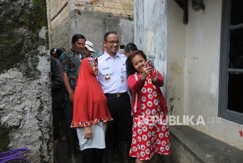 Gubernur DKI Jakarta Anies Baswedan berfoto bersama dengan warga seusai meninjau perbaikan tanggul Kali Pulo yang jebol akibat hujan ekstrem terjadi pada Senin (11/12) siang di Kelurahan Jatipadang, Pasar Minggu, Jakarta, Rabu (13/12).