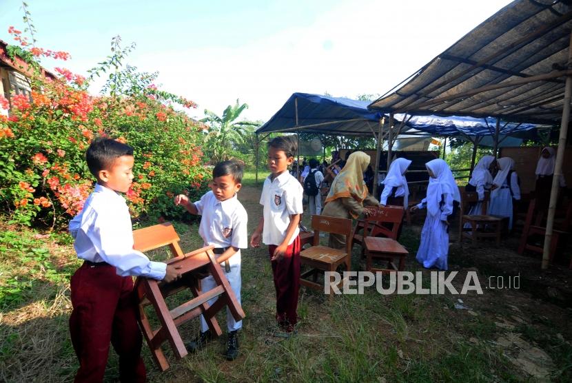 Sejumlah pelajar membawa bangku secara estafet untuk digunakan belajar di kelas tenda darurat pada hari pertama sekolah di SDN Mutiara, Desa Cibeber II, Leuwiliang, Kabupaten Bogor, Jawa Barat, Senin (16/7).