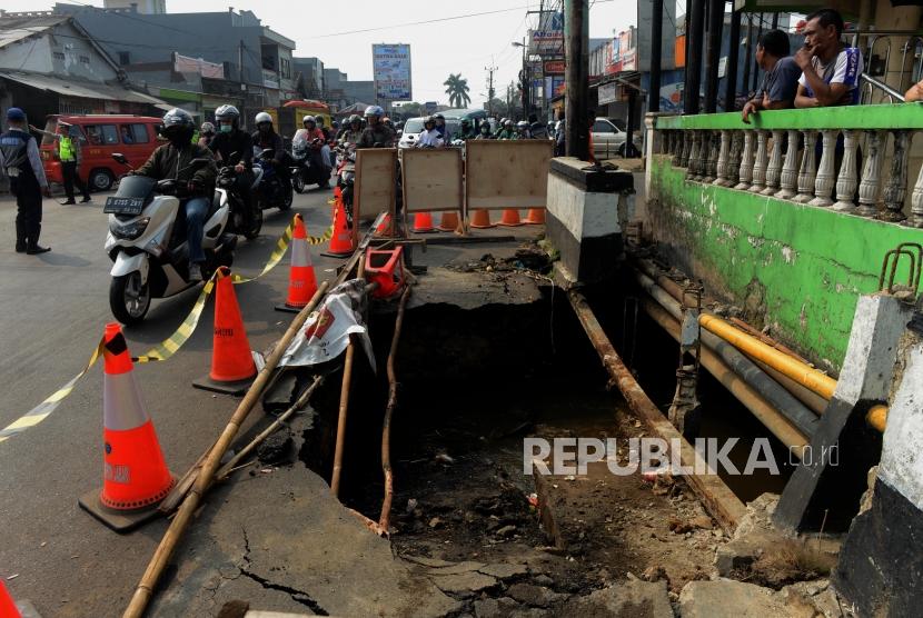 Pengendara motor melintas di dekat jalan yang amblas di Jalan Raya Sawangan, Depok, Jawa Barat, Jumat (28/6).