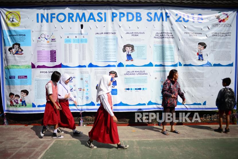 PPDB Kota Bandung. Siswa berseragam sekolah dasar melintasi baliho informasi Perimaan Peserta Didik Baru (PPDB) di SMPN 34 Bandung, Senin (2/7).