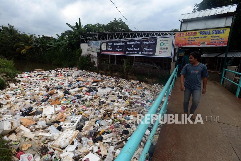 Warga berjalan di atas jembatan sungai yang aliran airnya dipenuhi tumpukan sampah di anak Sungai Ciliwung Kali Baru, Bojong Gede, Bogor, Jawa Barat, Kamis (31/1).