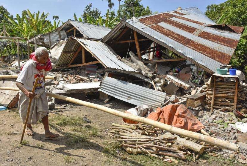 Warga berjalan di depan rumah yang roboh akibat gempa di Desa Sajang, Kecamatan Sembalun, Selong, Lombok Timur, NTB, Minggu (29/7).