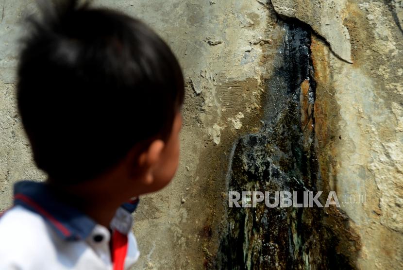 Anak-anak melihat air yang mengucur dari tanggul pengaman pantai yang bocor di kawasan Muara Baru, Jakarta, Selasa (11/12).