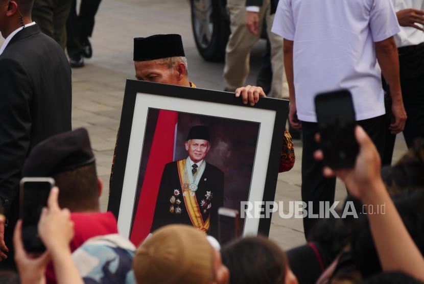 Seorang petugas membawa foto Presiden Ketiga RI BJ Habibie pelataran Taman Makam Pahlawan Kalibata, Jakarta, Kamis (12/9).
