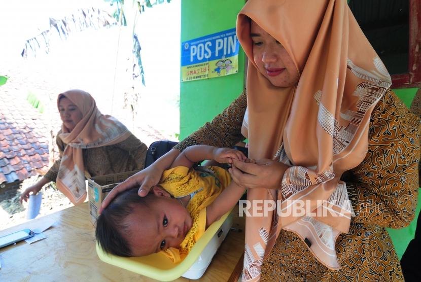 Petugas menimbang berat badan anak-anak sebelum pelaksanaan vaksin di Posyandu Desa Cibeber II, Leuwiliang, Kabupaten Bogor, Jawa Barat, Senin (16/7).