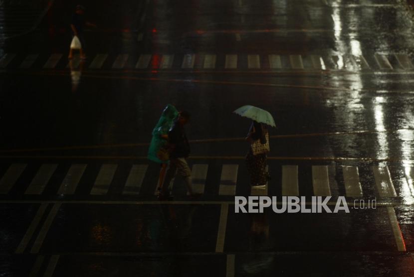 Sejumlah warga menyeberangi pelican crossing menggunakan payung saat hujan di Jakarta, Selasa (27/11).