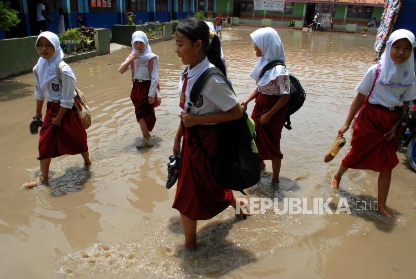 Sejumlah pelajar SD Negeri Keramat 2 melintasi genangan air yang merendam halaman sekolahnya, di Keramat, Pakuhaji, Kabupaten Tangerang, Banten.