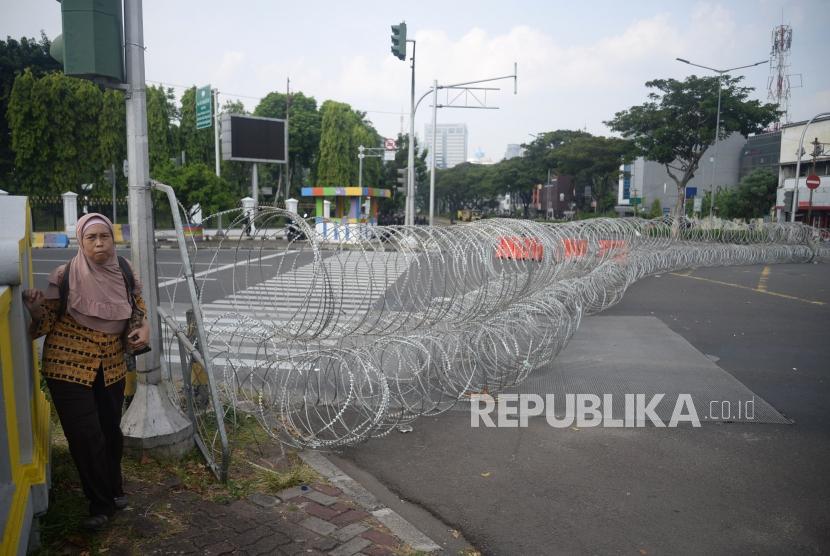 Pejalan kaki melintas didekat kawat berduri ketika adanya penutupan jalan dan pengalihan arus lalu lintas di Kawasan Harmoni, Jakarta, Jumat (14/6).