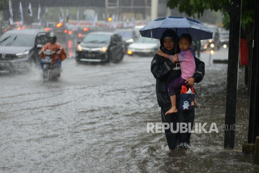 Warga melintasi genangan air saat terjadi banjir di kawasan Pancoran, Jakarta, Selasa (18/12).