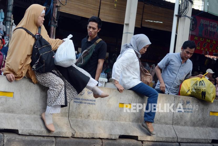 Warga melintasi pagar beton pembatas jalan di Jalan Jatibaru, Tanah Abang, Jakarta, Rabu (9/1).