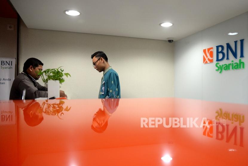 Petugas melayani transaksi nasabah di kantor layanan BNI Syariah, Jakarta, Senin (11/12).